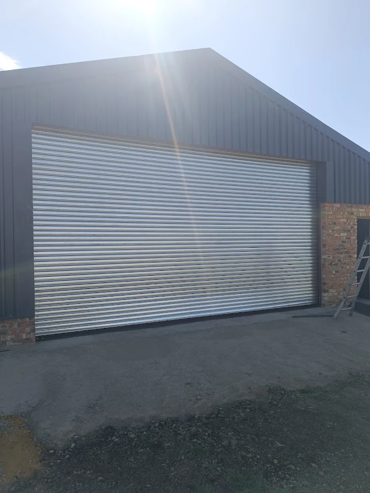 Very large black roller shutter door with worker standing beside it